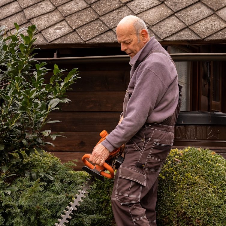 Älterer Herr hat Schwierigkeiten beim Hecke schneiden
